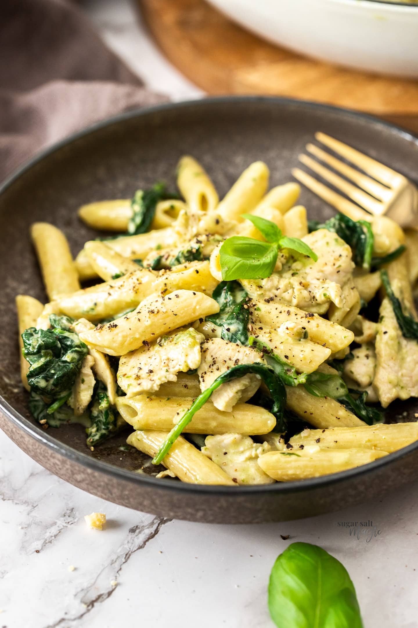 A brown bowl filled with creamy pasta chicken and spinach.
