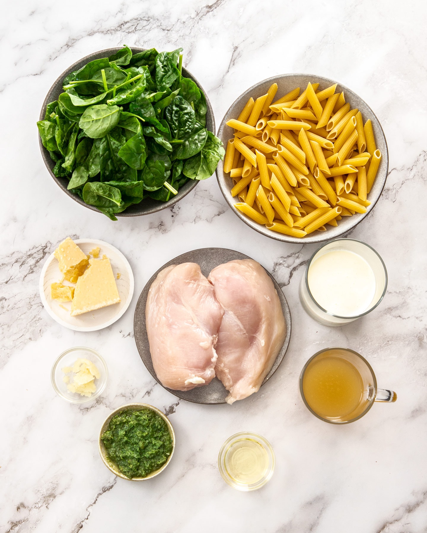 Ingredients for chicken spinach pasta on a marble surface.