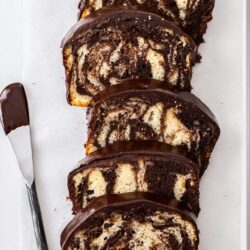 5 slices of marble cake on a tin with a ganache covered knife next to them.