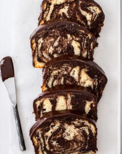 5 slices of marble cake on a tin with a ganache covered knife next to them.