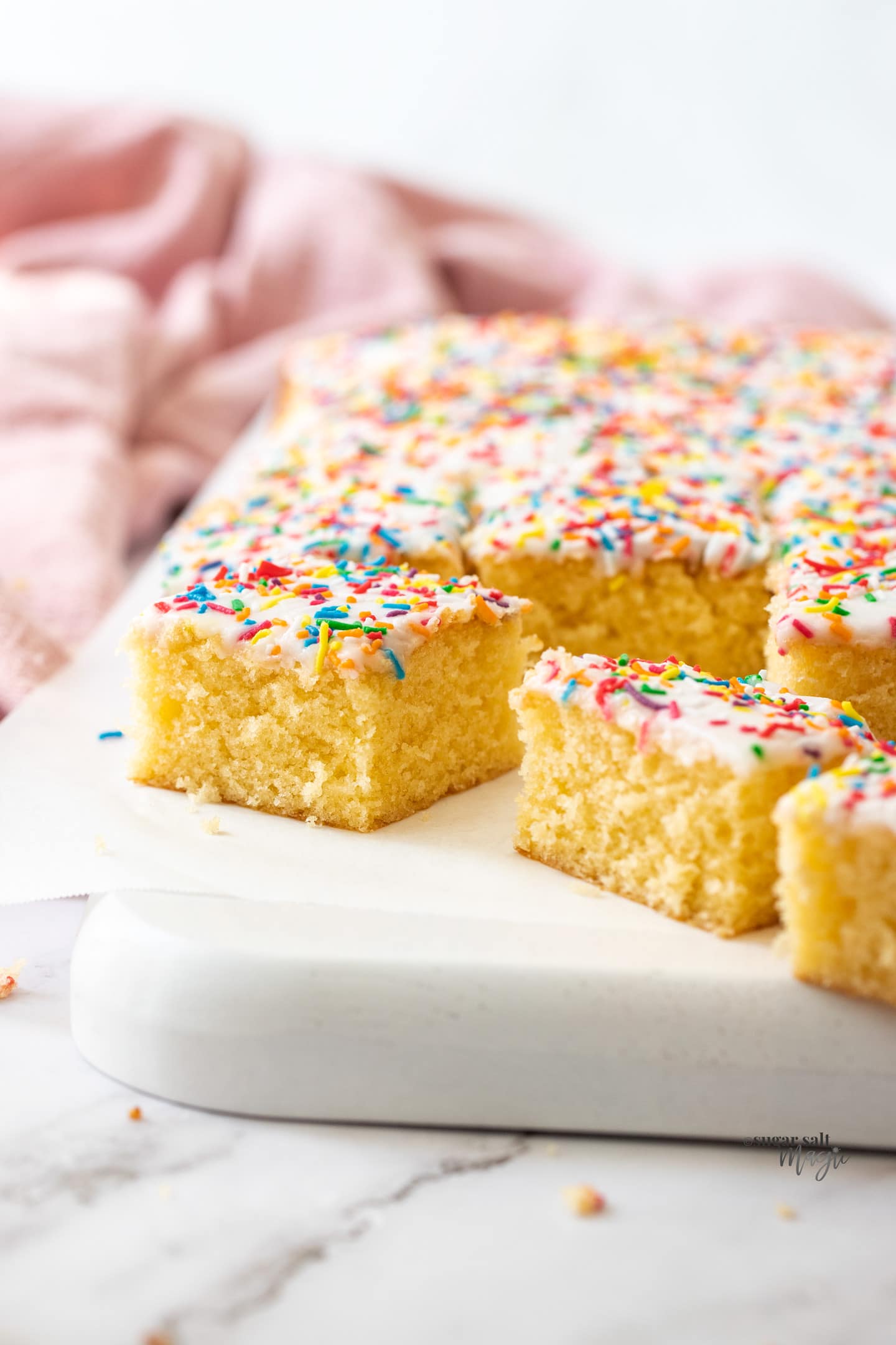 Squares of sponge cake topped with icing and sprinkles.