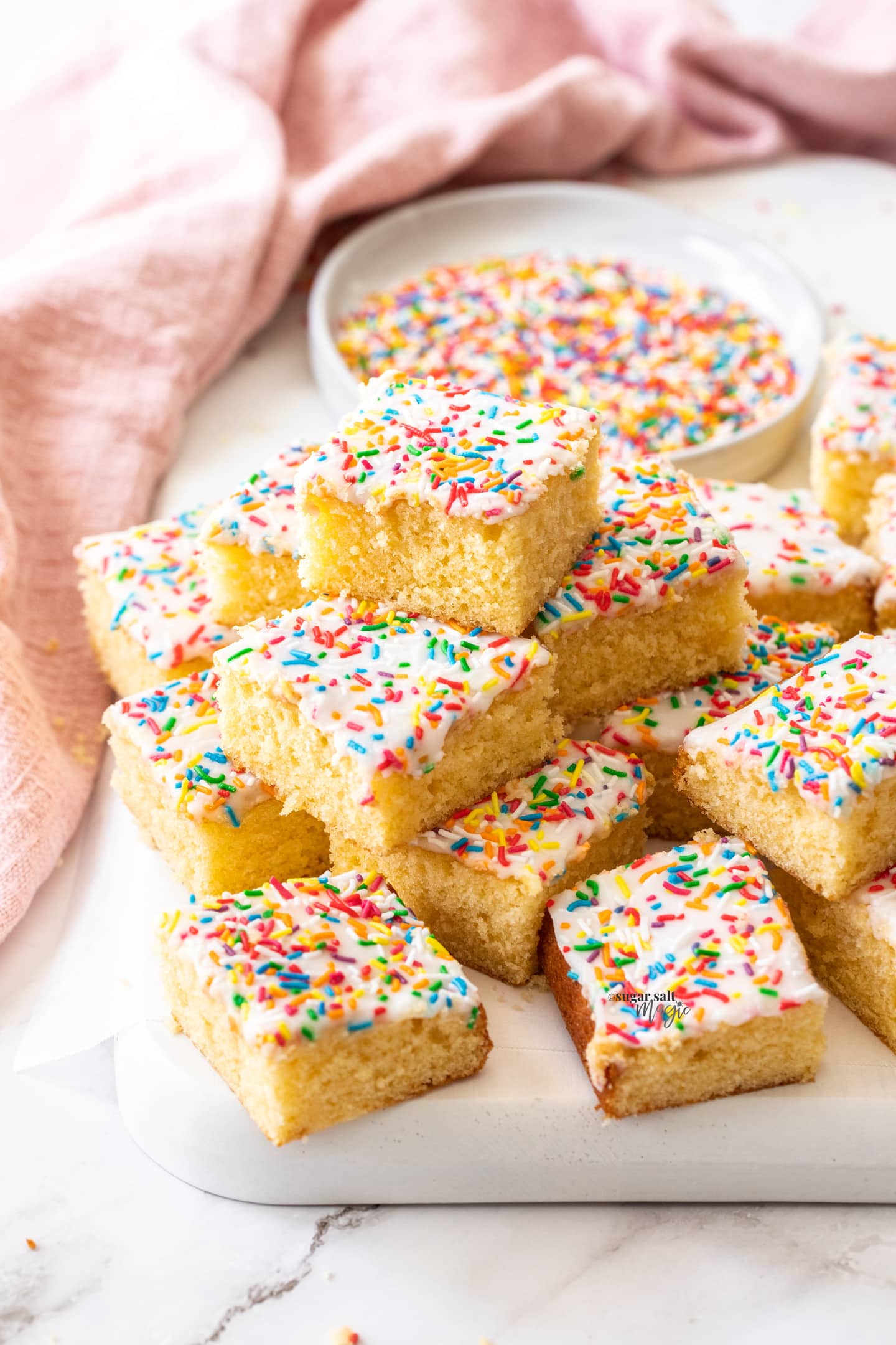 A stack of squares of sponge tray bake toped with sprinkles.