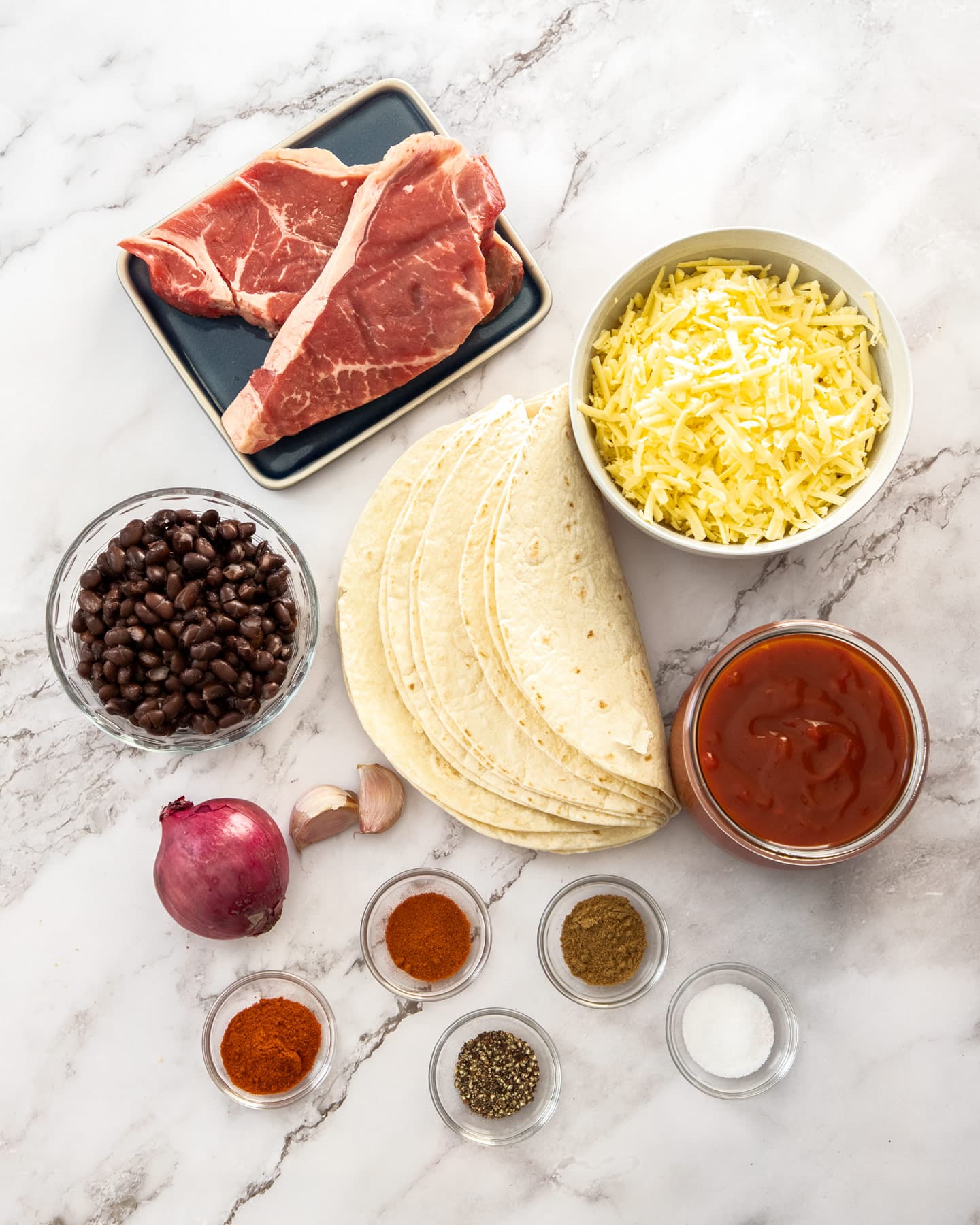 Ingredients for steak enchiladas on a marble surface.
