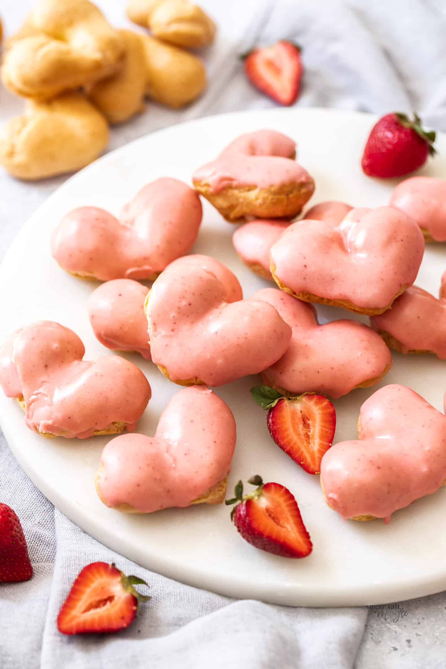 A pile of strawberry cream puffs on a white marble platter.