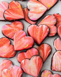 A pile of heart shaped iced sugar cookies on a stone surface.