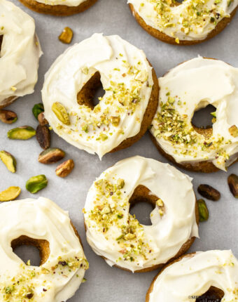 Closeup of 2 carrot cake donuts surrounded by pistachios.