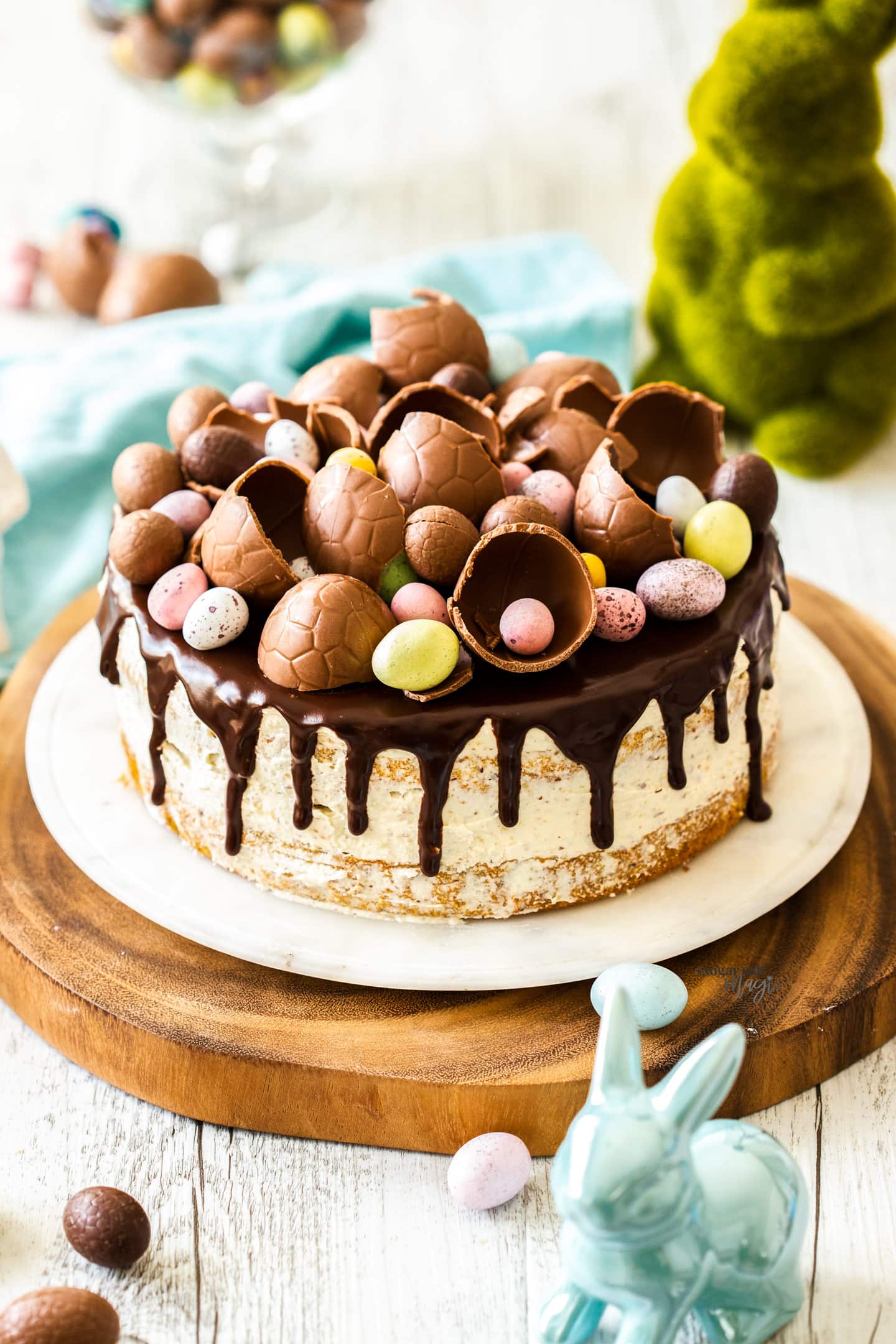 A whole cake, topped with ganache and easter eggs on a cake platter.