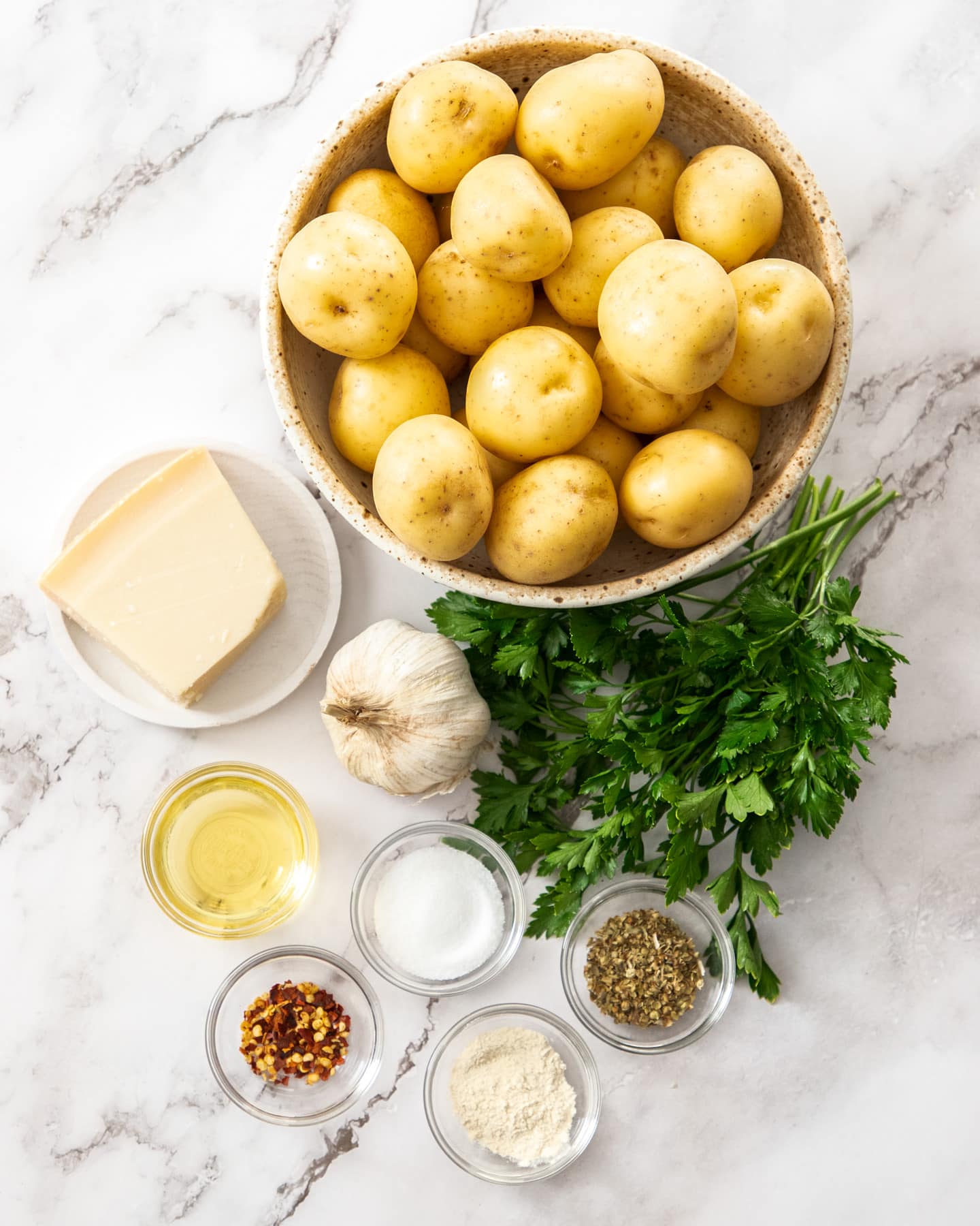 Ingredients for roasted parmesan garlic potatoes on a marble surface.