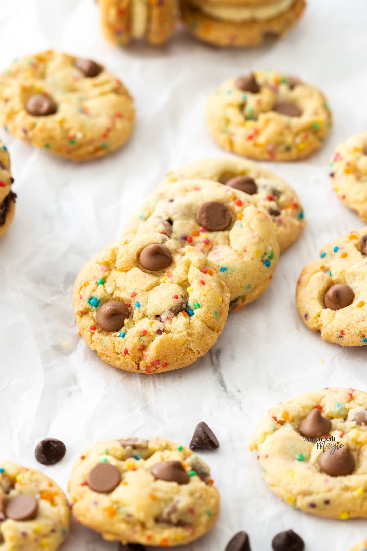 A batch of funfetti cookies with chocolate chips on a sheet of baking paper.