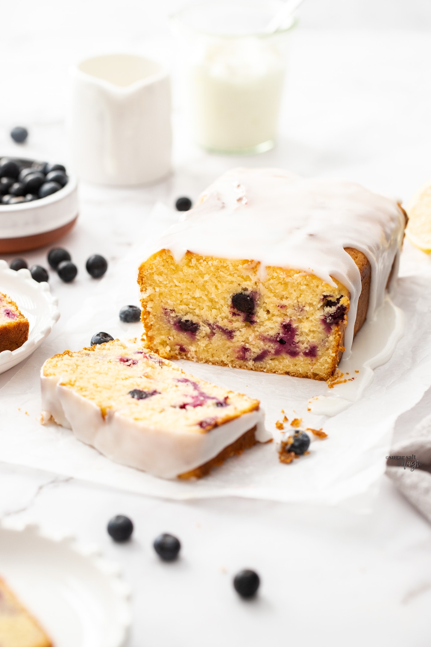 A lemon loaf cake, studded with blueberries with a slice cut away from it.
