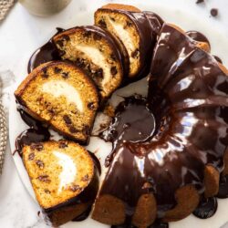 A sliced bundt cake topped with chocolate ganache on a marble platter.