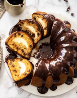 A sliced bundt cake topped with chocolate ganache on a marble platter.