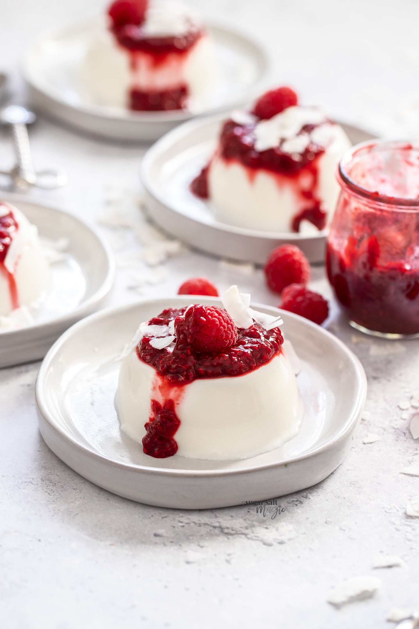 A coconut panna cotta topped with raspberry sauce on small grey dessert plate.