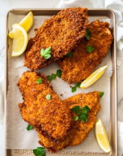 4 crunchy golden brown schnitzels on a baking tray with lemon wedges.