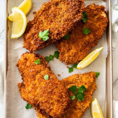 4 crunchy golden brown schnitzels on a baking tray with lemon wedges.