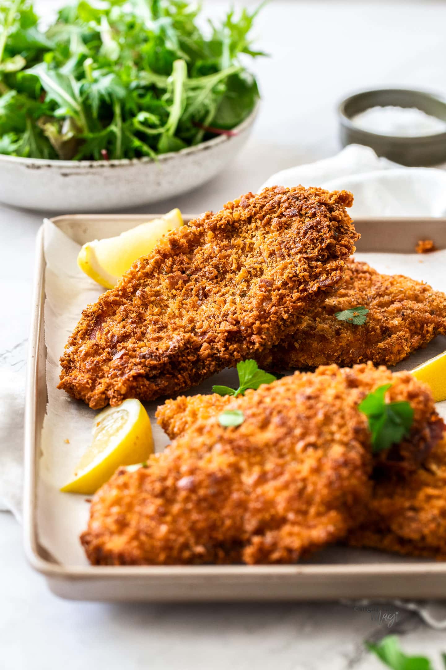 Crunchy golden brown schnitzels on a baking tray with lemon wedges.