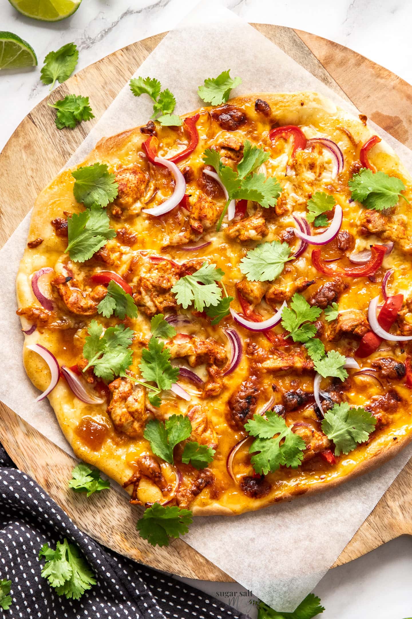 A whole tandoori chicken pizza on a wooden serving board.