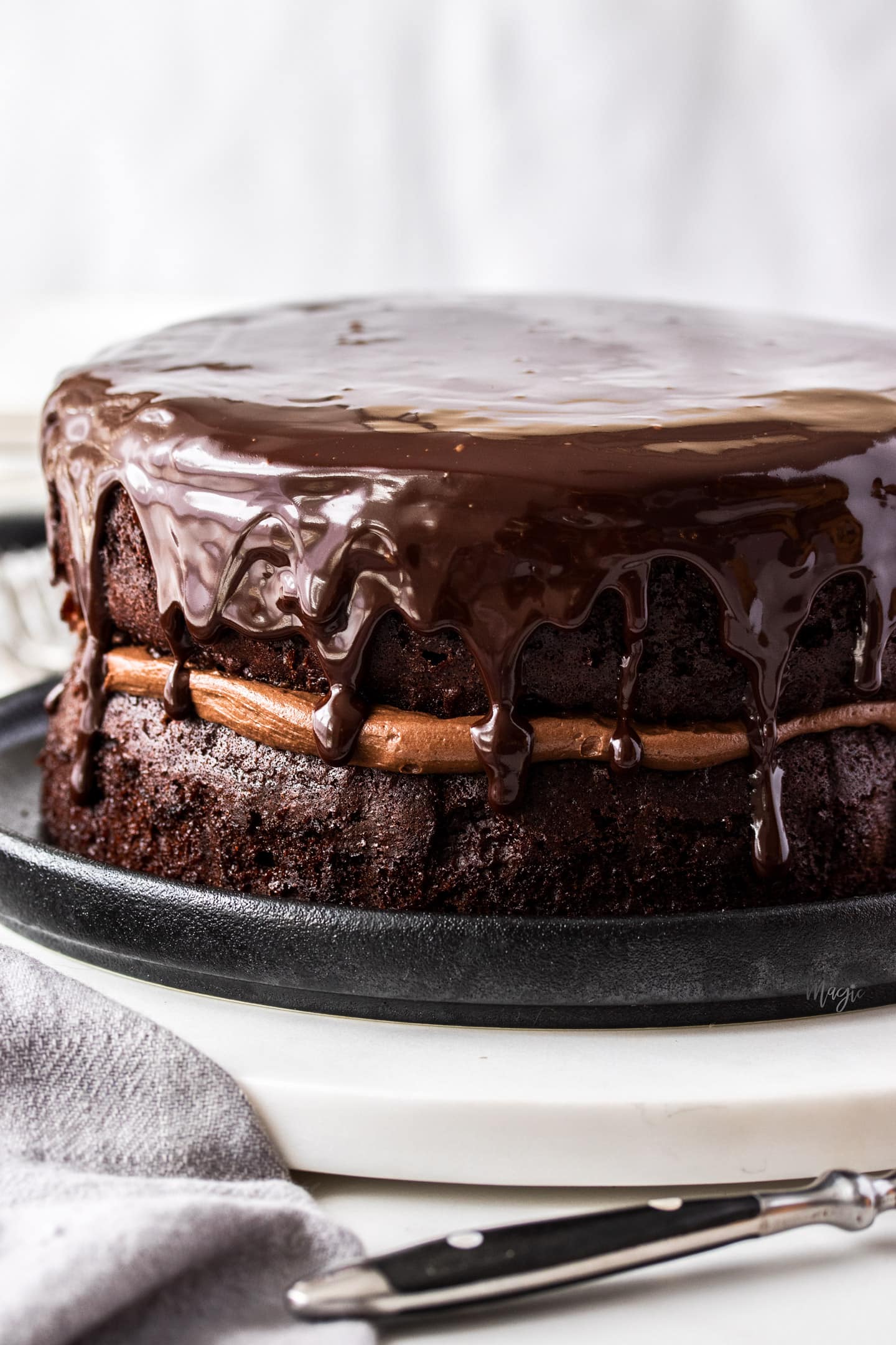 A chocolate cake topped with ganache on a marble platter.