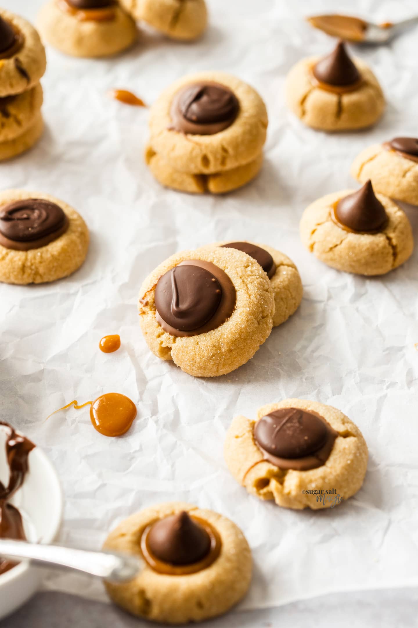 A batch of caramel peanut butter thumbprint cookies on a sheet of baking paper.