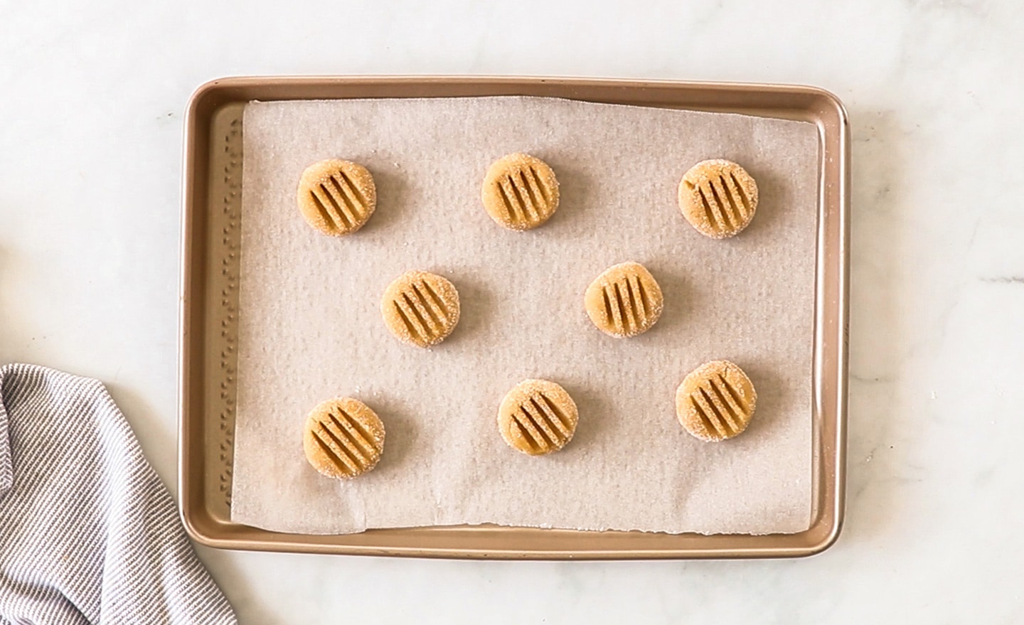 Balls of cookie dough on a sheet press with a fork to create a pattern on top.