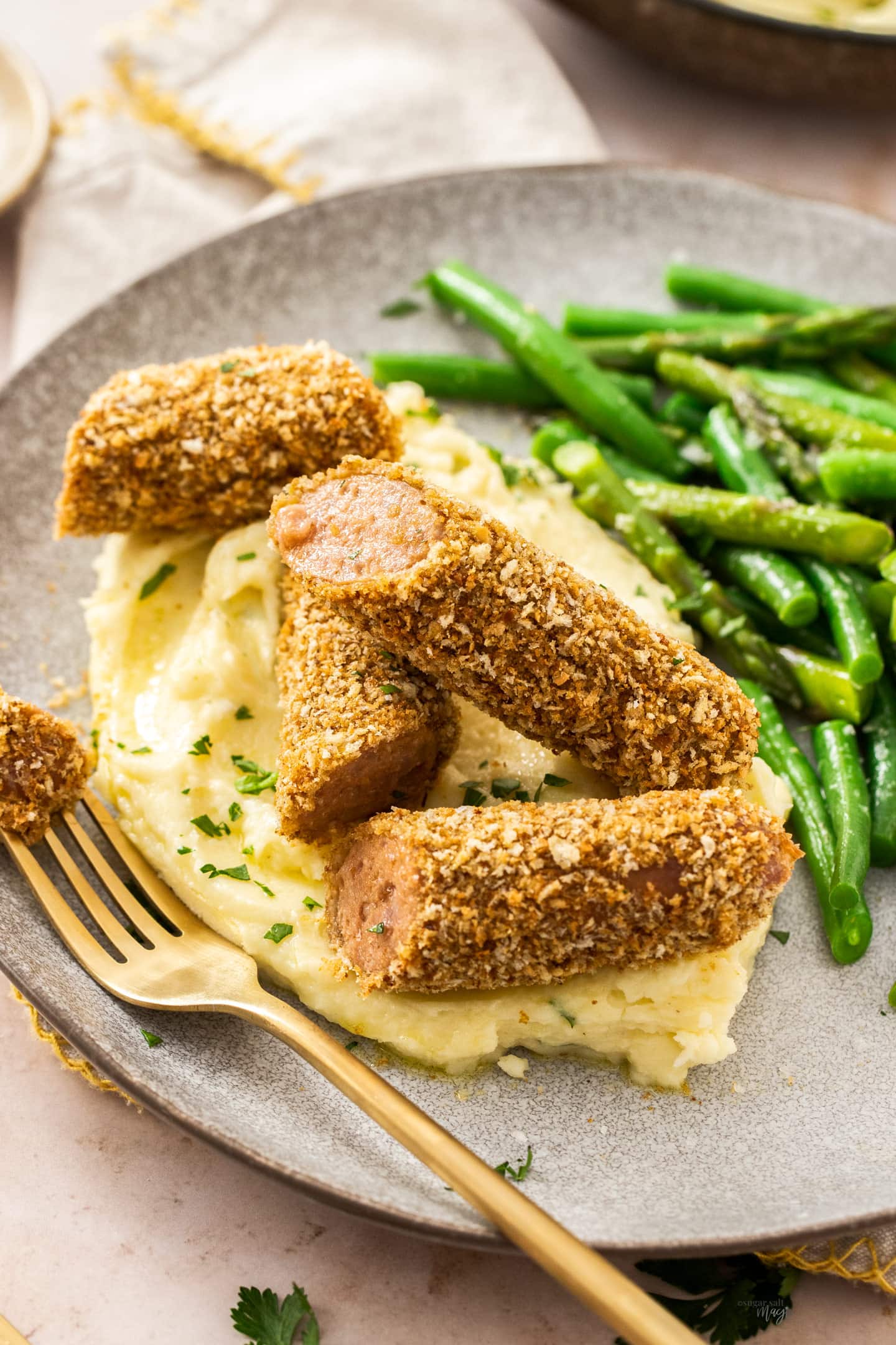 Closeup of cut up crumbed sausages on top of mashed potato.
