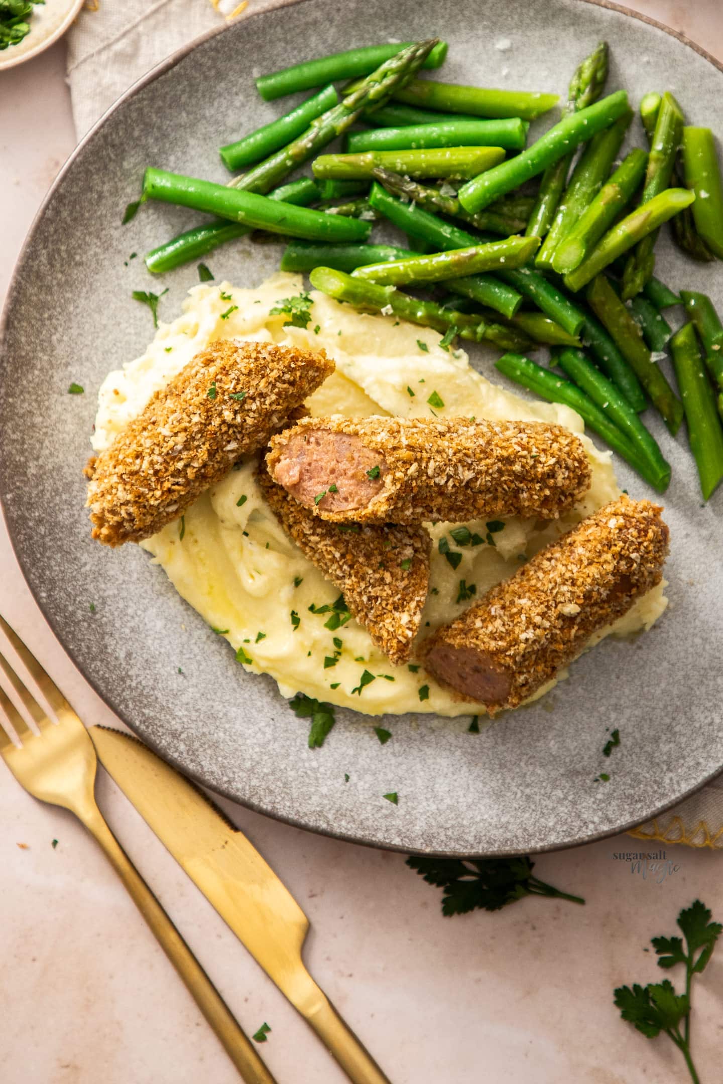 Crumbed sausages cut into pieces on a pile of mashed potato with beans to the side.