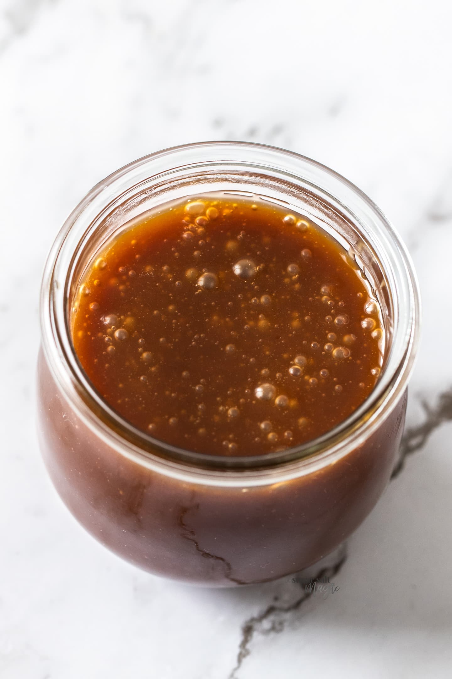 A round glass jar filled with caramel sauce.