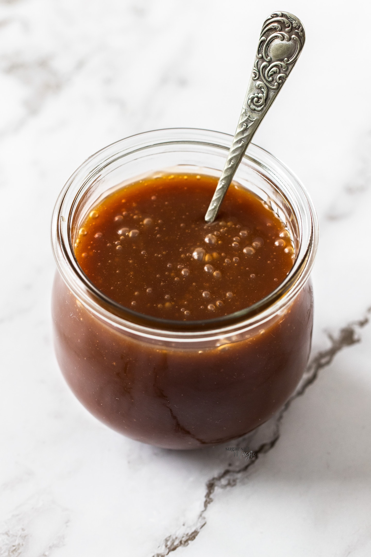A round glass jar filled with caramel sauce with a spoon sticking out.