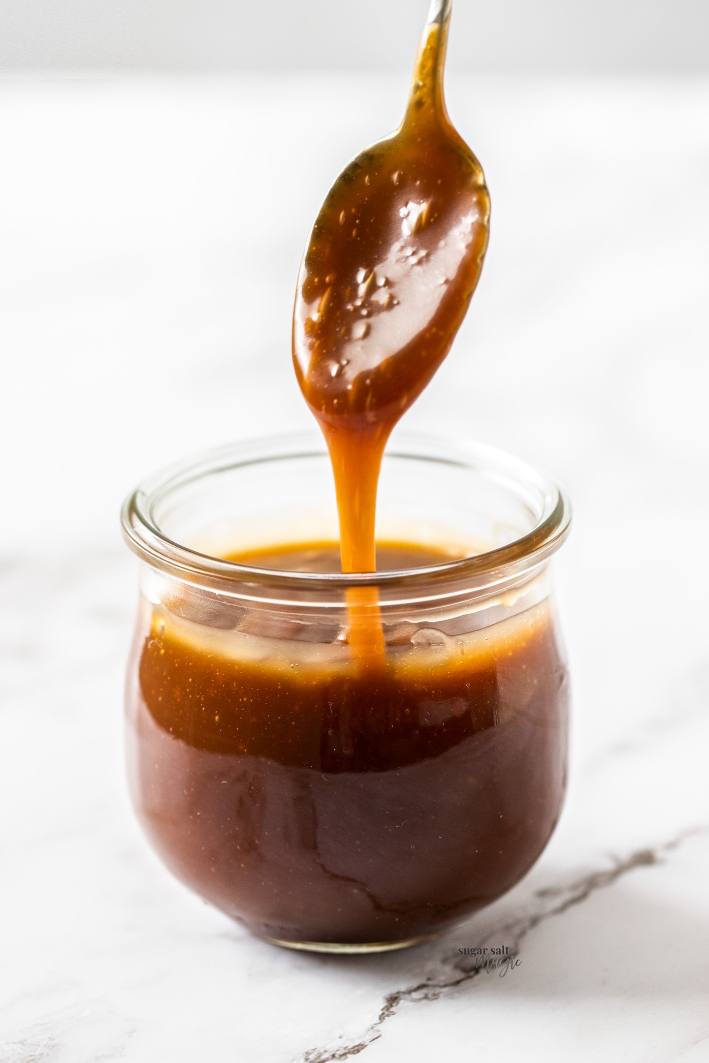 Caramel pouring off a spoon into a glass jar.