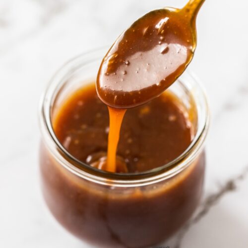 A spoon coated with caramel sauce, hovering over a jar.