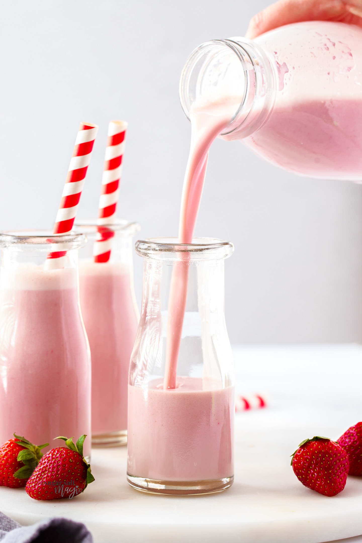 Strawberry milk being poured into a miniature milk bottle.