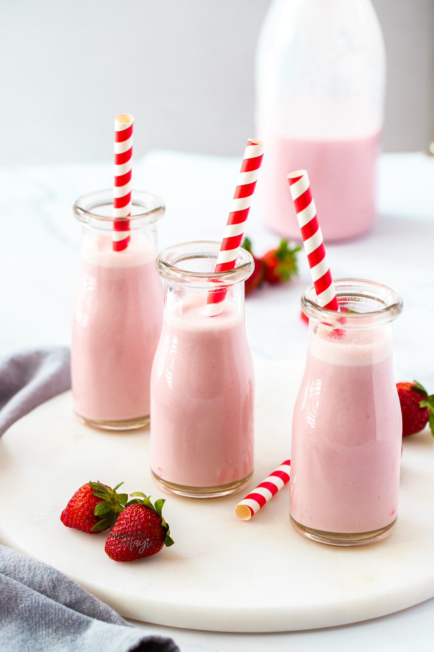 3 miniature milk bottles filled with strawberry milk with stripy red straws.