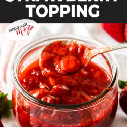 A glass pot of strawberry topping with a spoon taking some out.