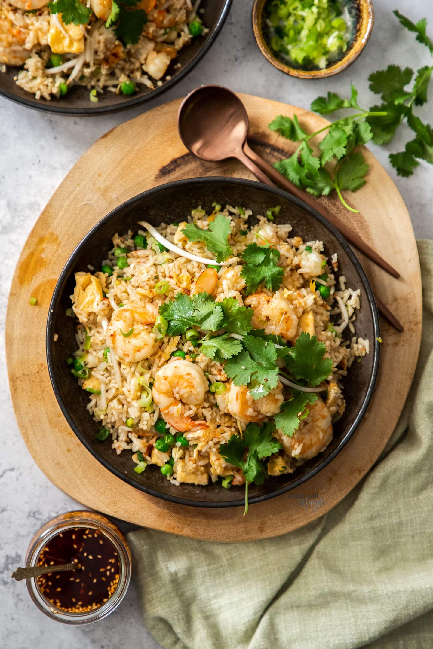 Top down view of a bowl of prawn fried rice on a wooden platter with spoons.