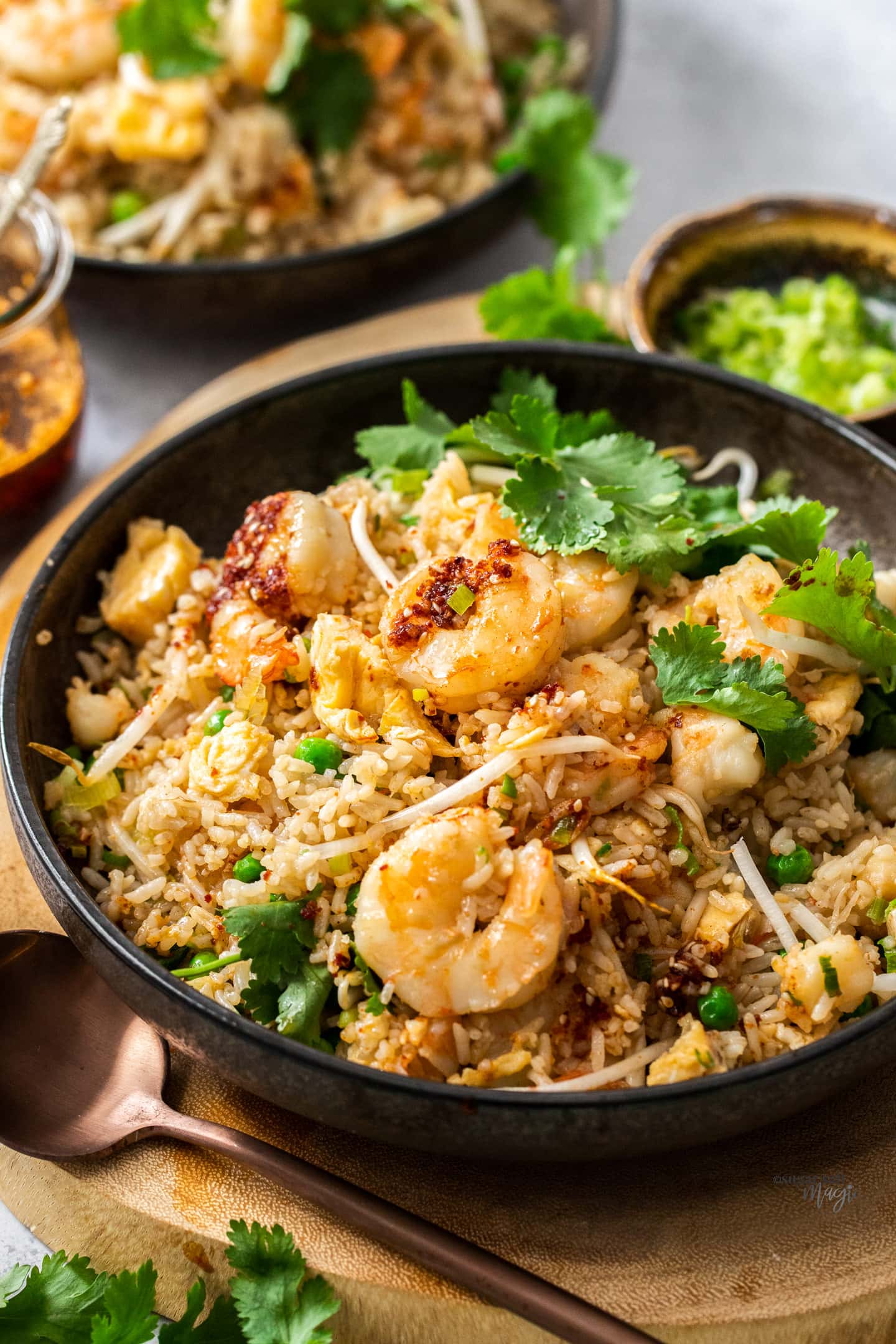 A bowl of prawn fried rice with a spoon in front.