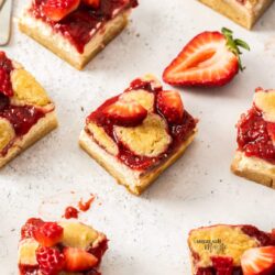 A batch of strawberry topped cheesecake bars cut into squares.