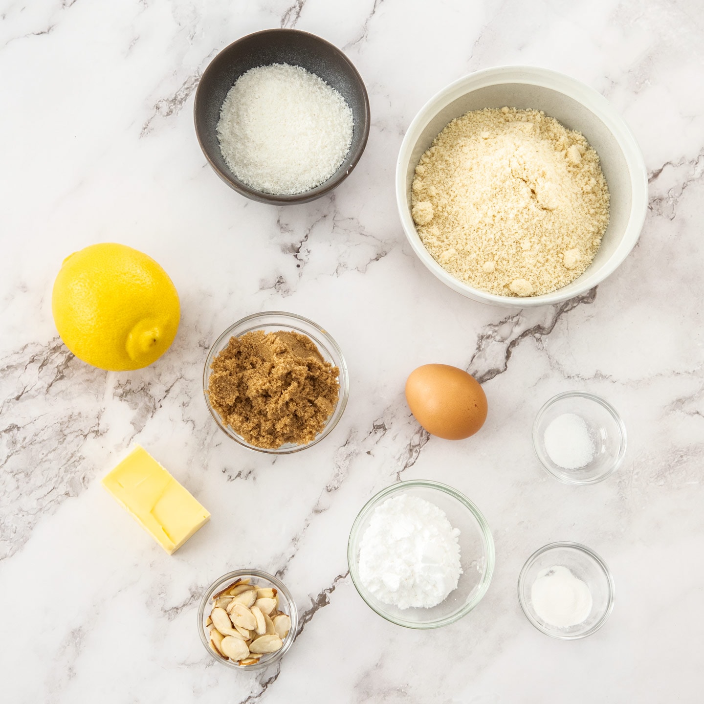 Ingredients for almond coconut cookies on a marble surface.