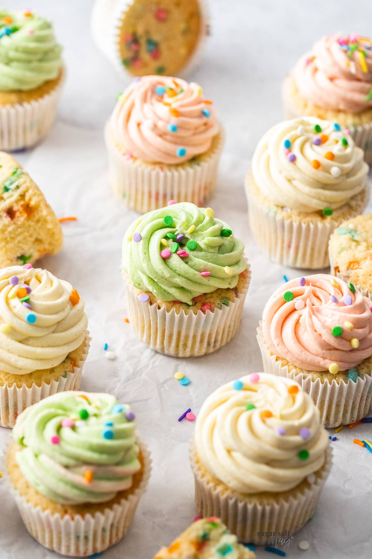A batch of 12 confetti cupcakes with different coloured frosting.
