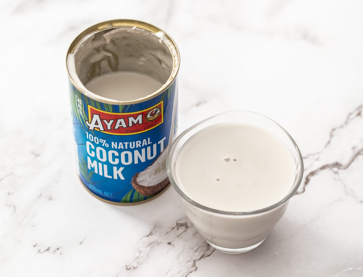 A can of coconut milk, next to a glass full of it.