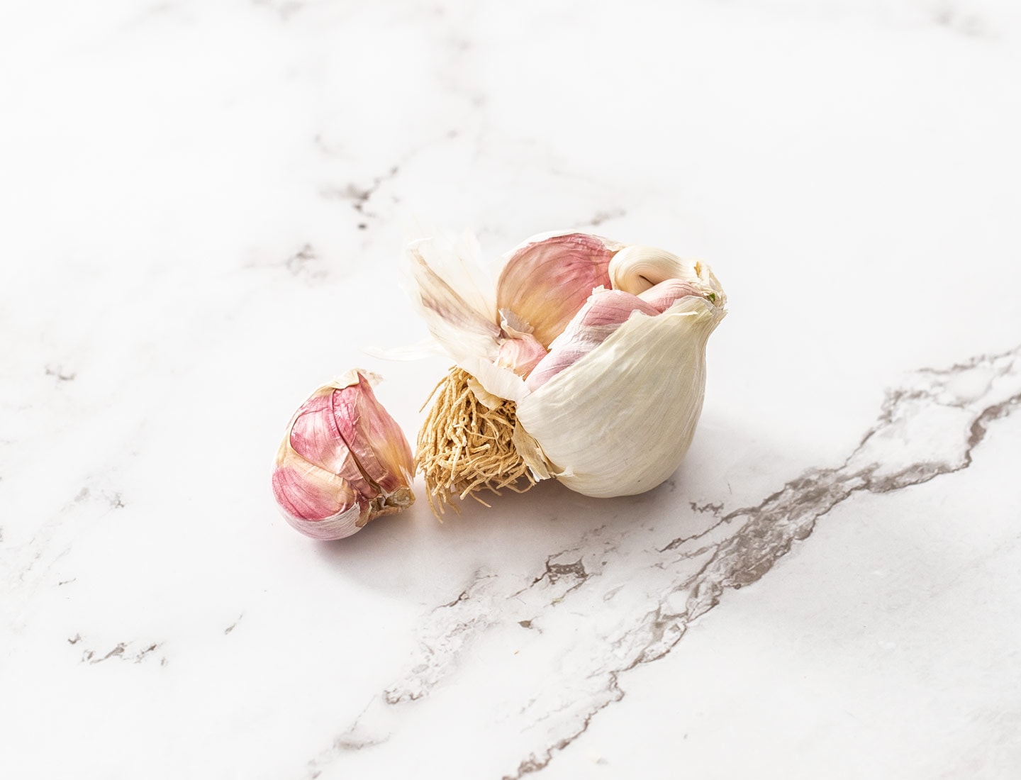 A bulb of fresh garlic on a marble surface.