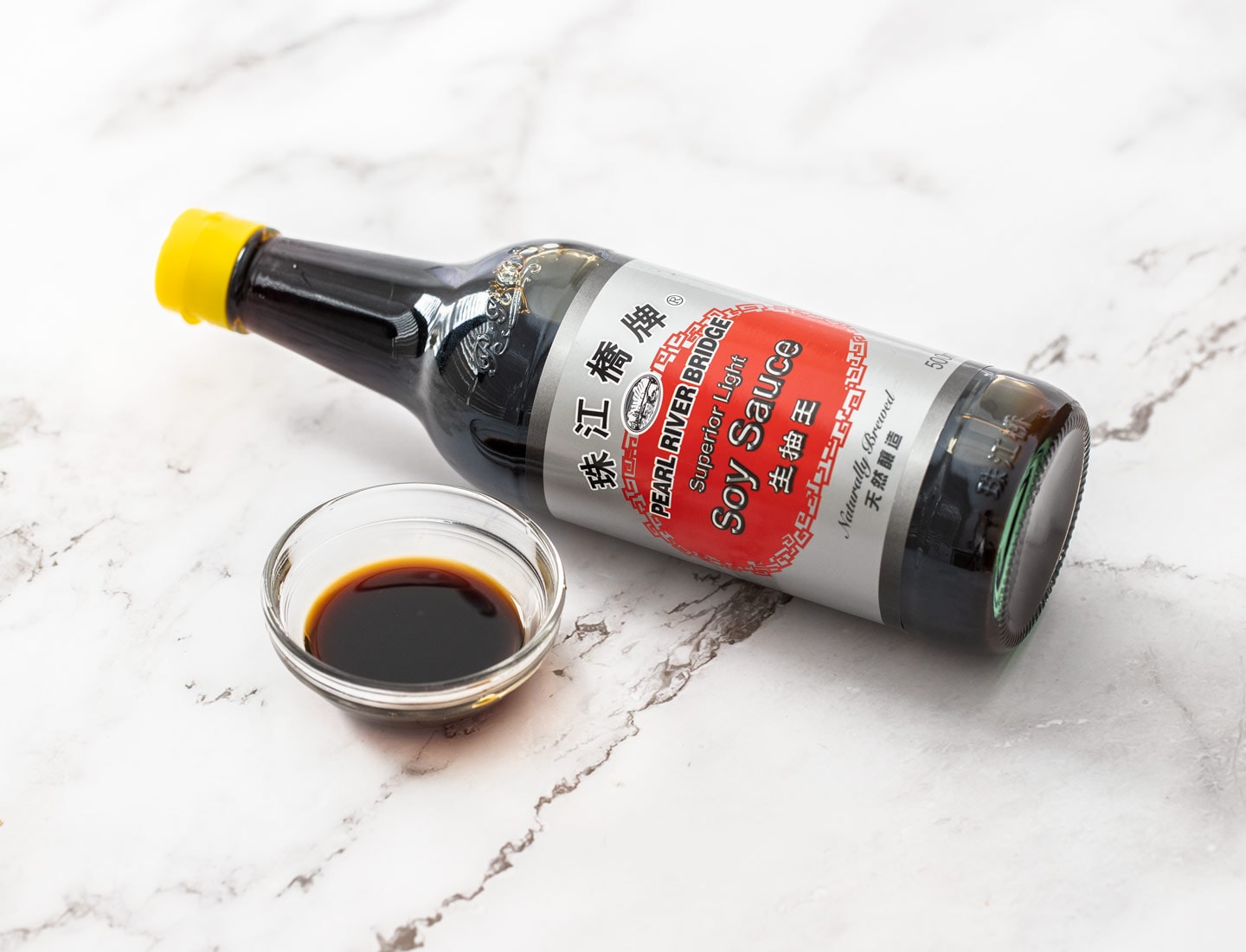 A bottle of soy sauce next to a small dish of it.