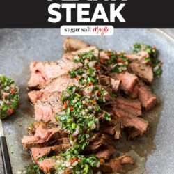 A thinly sliced steak topped with chimichurri on a grey dinner plate.