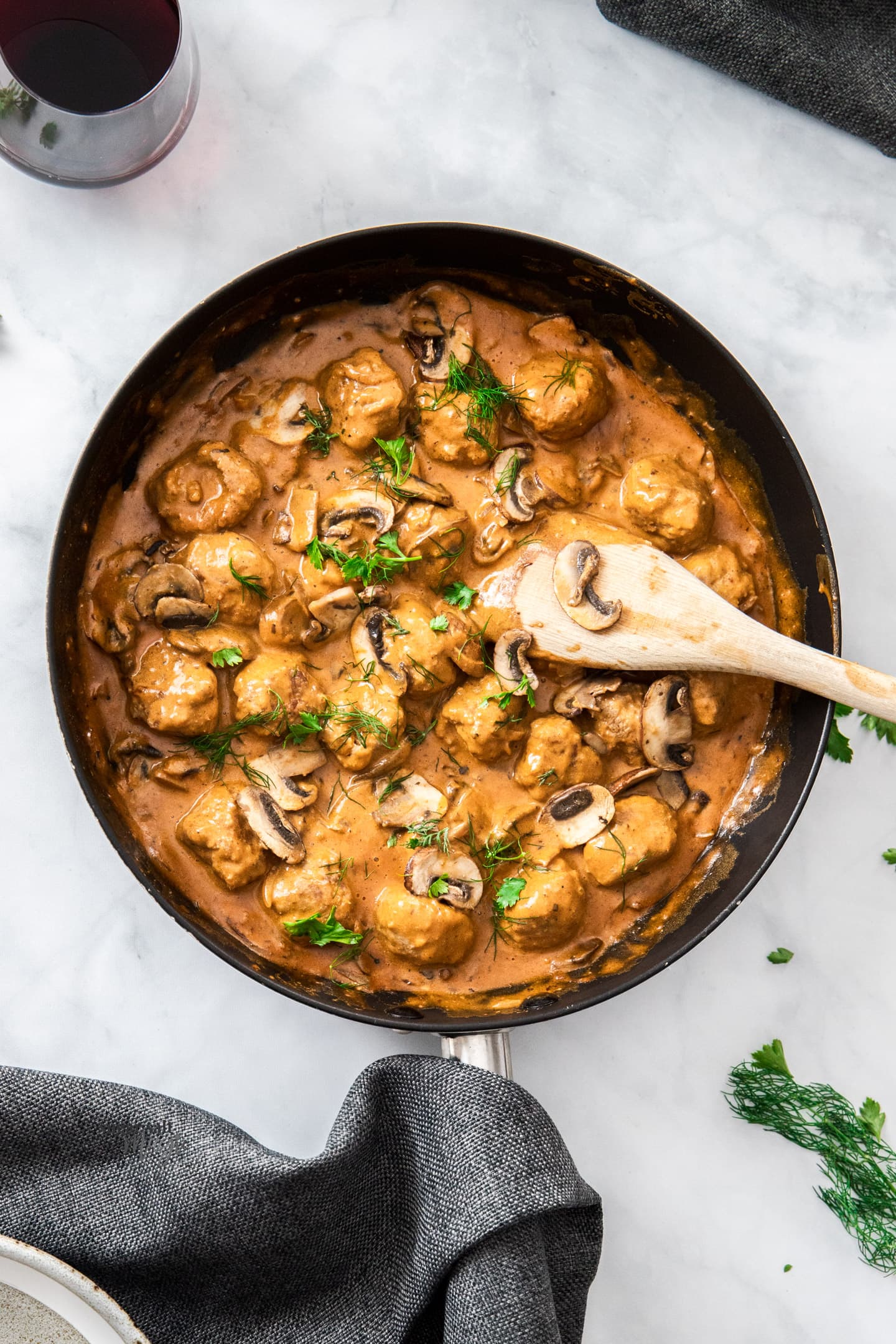 A large skillet filled with meatball stroganoff with a wooden spoon.