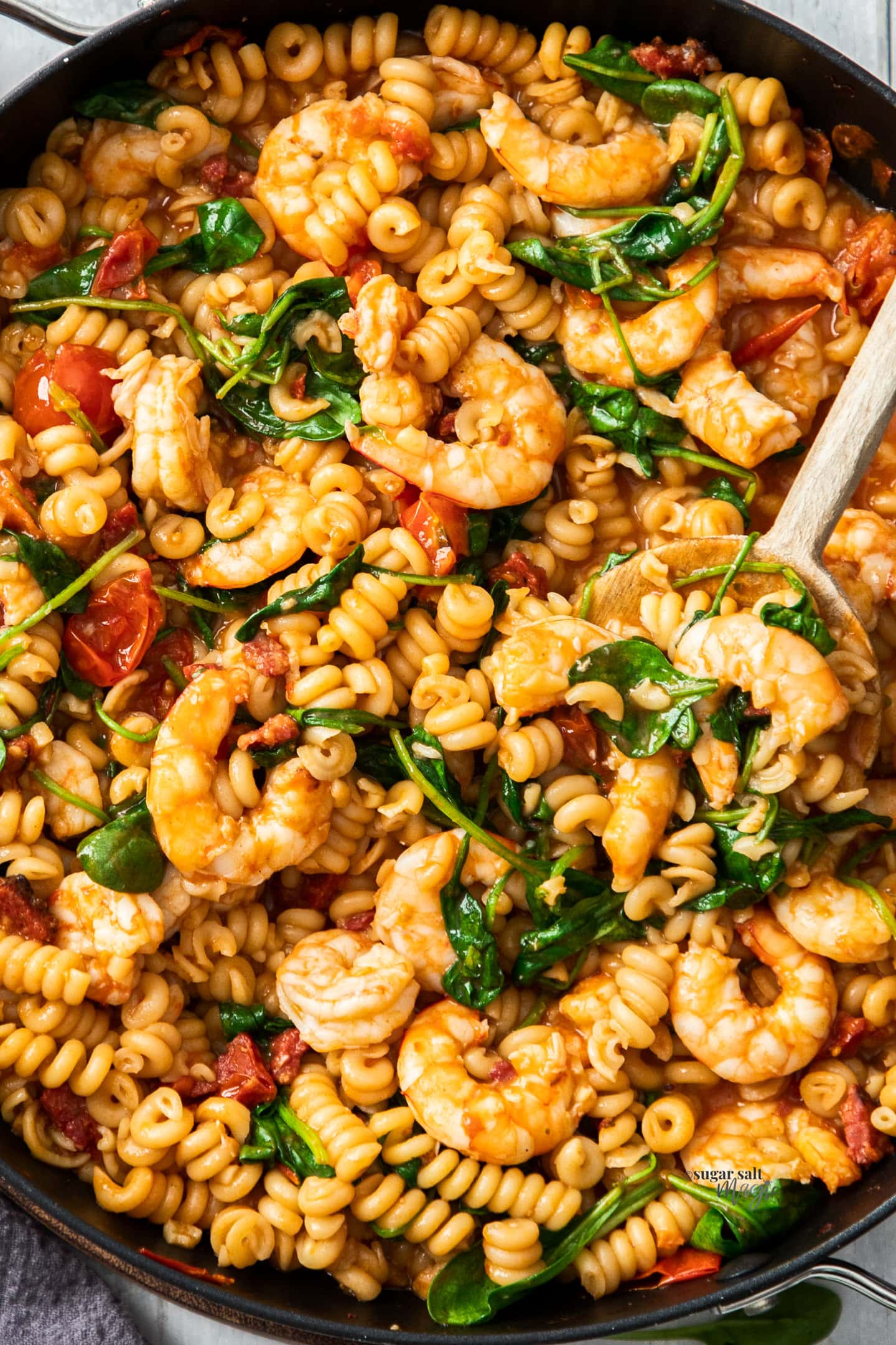 Closeup of prawns, spinach and pasta in a large skillet.