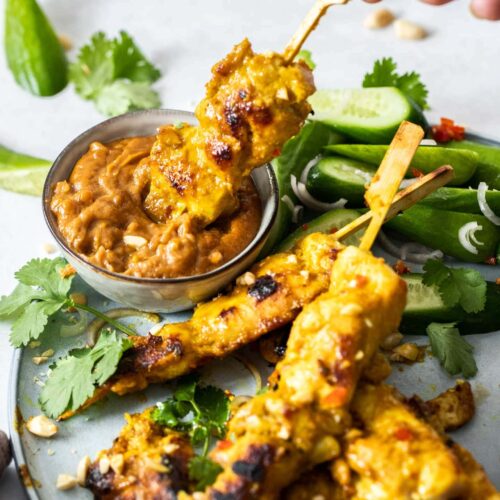 A skewer of chicken satay being dipped into peanut sauce.