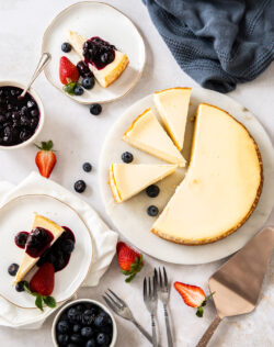 Top down view of a cheesecake cut up and some slices on dessert plates.