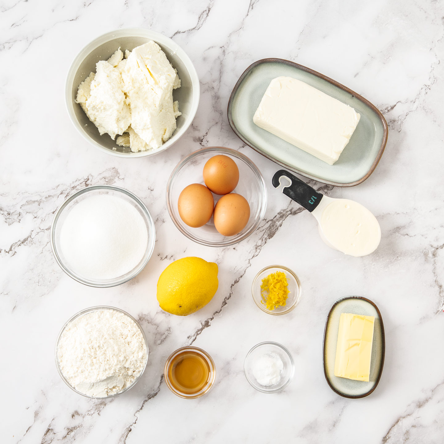 Ingredients for baked ricotta cheesecake on a marble surface.