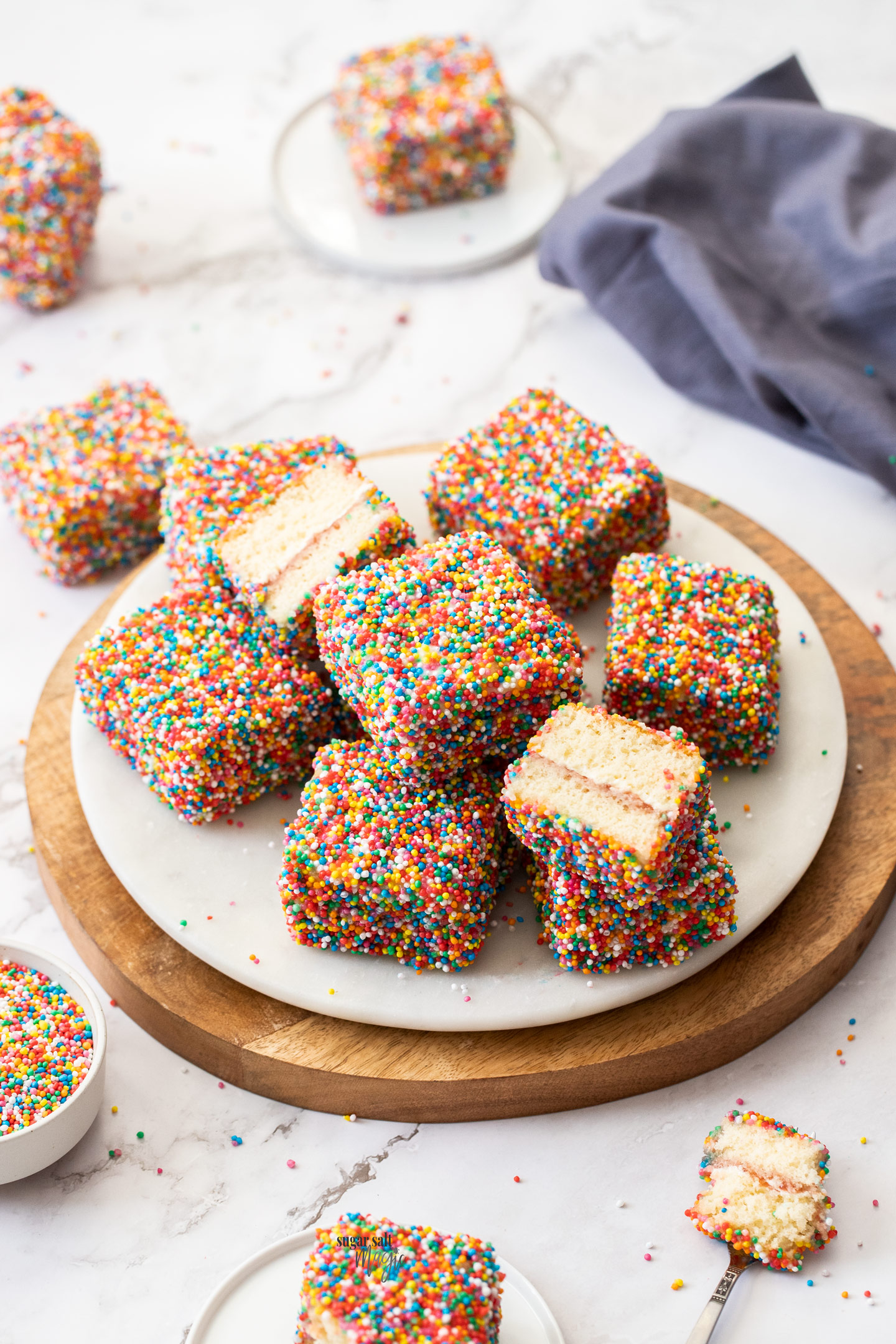 A batch of fairy bread lamingtons on a marble serving platter.