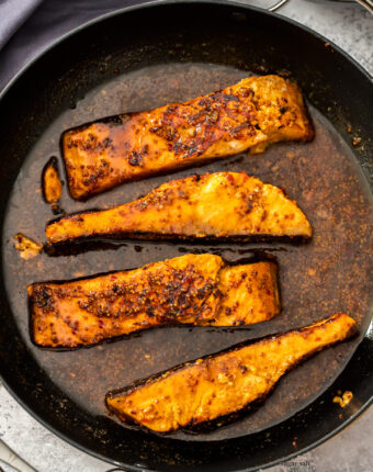 A large skillet filled with 4 pieces of salmon in sauce.