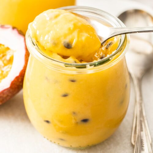 A spoon taking passionfruit curd out of a jar.